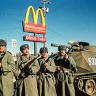 McDonald's-Schild mit "OVER 45 BILLION SERVED". Vier Personen in Uniformen neben einem Militärfahrzeug.