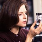 Eine Frau hält ein kleines Glas mit dunklem Inhalt konzentriert in der Hand.