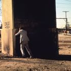 Graffiti mit Text "CONEJO and WE" und "VOTE NO ... BROWN" auf Betonwand. Drei Männer in urbanem, industriellem Umfeld.