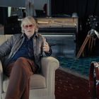 Ein älterer Mann mit Sonnenbrille sitzt lässig in einem Sessel. Im Raum stehen ein Flügel, eine Kamera und ein Schlagzeug.