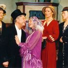 Fünf Personen in historischen Kostümen stehen zusammen; ein Mann im Zylinder umarmt eine Frau in einem lila Federkleid.