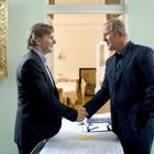 Zwei Männer schütteln sich die Hand. Im Hintergrund sind ein Gemälde einer Frau und ein Landschaftsbild.