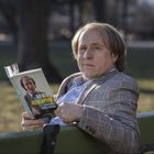 Person in einem Anzug sitzt auf einer Bank und liest ein Buch mit dem Titel: "Du bist kein Opfer". Im Hintergrund ist ein Park.