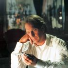 Ein Mann in einem weißen Hemd betrachtet nachdenklich ein glitzerndes Modell eines Schmetterlings in seiner Hand.