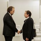 Zwei Männer in Anzügen geben sich in einem öffentlichen Waschraum die Hand. 