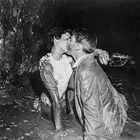 Ein Paar küsst sich innig auf dem Boden einer dunklen und schlammigen Umgebung. Sie wirken emotional verbunden.