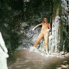 Eine Frau steht vor einer Felswand, trägt einen orange gemusterten Anzug und lehnt lässig gegen den Felsen.