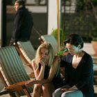 Zwei Frauen auf Liegestühlen; eine tröstet die andere. Im Hintergrund geht ein Mann vorbei.