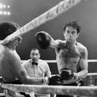 Zwei Boxer im Ring, der rechte schlägt den linken. Ein Schiedsrichter beobachtet den Schlag.