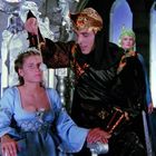 In einer fantasievollen Szene sitzt eine Frau in einem blauen Kleid auf einem Thron, während ein Mann in exotischem Gewand steht.