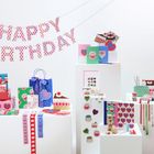 „HAPPY BIRTHDAY“ Buchstaben oben, bunte Geschenkverpackungen, Herzen und Kuchenmotive auf weißen Sockeln.