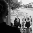 Eine Frau sieht aus einem Fenster, draußen stehen mehrere ernste Kinder in traditioneller Kleidung.