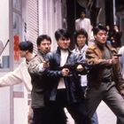 Rote Schriftzeichen an den Fenstern. Sechs Männer, vier mit Waffen, gehen entschlossen die Straße entlang. Stadtumgebung.