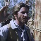 Ein Mann in historischer Kleidung steht vor einem Baumstamm mit Seilen. Menschen im Hintergrund heben die Hände.