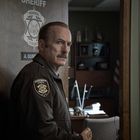 Auf der Tür steht "Sheriff, Normal County, A. Gunderson". Eine Person in Uniform hält einen Donut und schaut ernst.
