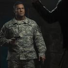 Ein Mann in Militäruniform mit den Aufschriften „Reacher“ und „U.S. Army“ hält eine Pistole.