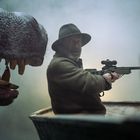 Eine Person mit Hut und Gewehr sitzt in einem Boot, bedroht von einem großen, furchteinflößenden Tiermaul.