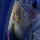 Der Schriftzug "Airlines Vero" ist auf einer Kopfstütze zu sehen. Ein älterer Mann mit langem Haar schaut aus einem Flugzeugfenster.
