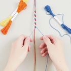 Zwei Hände knüpfen ein buntes Freundschaftsarmband. Links und rechts liegen bunte Stickgarne bereit.