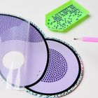 Kreisförmiges, lilafarbenes Bastelmaterial mit kleinen, lila Perlen und einem pinken Stift daneben auf hellem Hintergrund.