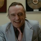 Zwei unscharfe Schallplatten im Hintergrund, Mann in einem hellen Anzug lächelt freundlich in die Kamera.
