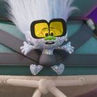 Ein kleiner, glitzernder Charakter mit großer Sonnenbrille klammert sich an einen plüschigen, bunten Hintergrund.