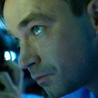 Links ein Mann mit Kopfhörer, rechts ein Mann in blauem Licht, intensiv fokussiert.