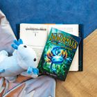 „THE LAST IMMORTALS: DAWN OF THE AXOLOTL“ von Kit Brooks. Ein blaues Stofftier und Buch auf Decken liegend.
