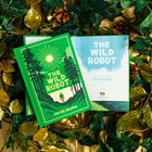 "The Wild Robot" von Peter Brown; grüne und blaue Buchcover in einem Arrangement mit goldenen und grünen Blättern.