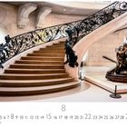 "Treppenhaus" steht unterhalb einer eleganten Treppe mit kunstvollem Geländer und einer Skulptur rechts davon.
