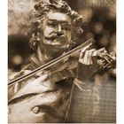 Text: "JOHANN STRAUSS." Sepiafarbene Statue eines Mannes mit Geige. Unter ihm ein Monatskalender, August.