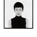 Eine Person mit kurzem schwarzen Haar trägt einen schwarzen ärmellosen Rollkragenpullover vor weißem Hintergrund.