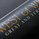 Text: "WEST OF WIC... GREAT AND TERRIBLE". Goldene Buchstaben auf dunklem Hintergrund, möglicherweise ein Buchcover.