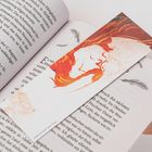 Ein Lesezeichen mit flammendem Haarmotiv liegt in einem geöffneten Buch, Text beginnt mit "Es war". Seiten sind deutsch beschriftet.