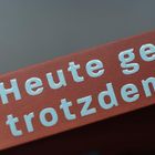 „Heute geh ich trotzdem r“ auf einem roten Hintergrund mit einem unklaren grauen Bereich darüber.