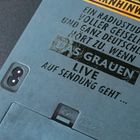Warnhinweis: Ein Radiostudio voller Geiseln… Live auf Sendung. Davor ein altes, blaues elektronisches Gerät.