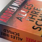 Auf dem Buchcover steht "ALLES IHRE SCHULD" in großen Buchstaben. Ganz oben "ANDREA MA", links am Buchrücken verkehrt.