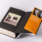 Ein Buch mit einem orangen Einleger, Text über einen britischen Autor. Links ein schwarz-weißes Foto von drei Personen.