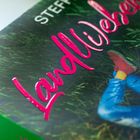 Der Text "Landliebe" in pinker Schrift. Sichtbar ist ein Bein in blauer Hose und rotem Schuh auf grünem Gras.