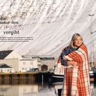 „Wo die Natur den Rhythmus vorgibt.“ Frau in Decke, Hafen, schneebedeckte Berge im Hintergrund, Boote.