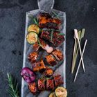 Es gibt keinen Text. Gegrillte Rippchen und Zucchini auf grauem Brett mit Rosmarin und Holzspießen.