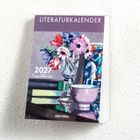 "LITERATURKALENDER 2027 Tageskalender ANACONDA" Ein Buch-Cover, bunte Blumen in einer Vase, Bücherstapel, Gemälde im Hintergrund.