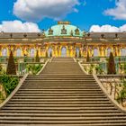 Breite Steintreppe führt zu großem Schloss mit gelber Fassade, grüner Kuppel, verzierten Fenstern und Gartenanlagen.