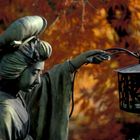 Eine Bronzestatue einer Frau im Kimono hält eine Laterne. Hintergrund: leuchtend rote Ahornblätter.