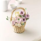 Ein Korb mit gehäkelten Blumen in Pastellfarben auf einem Tisch, Hintergrund unscharf mit Teekanne und Schalen.