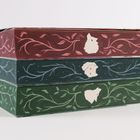 Drei gestapelte Bücher mit floralen Mustern und Silhouetten von Tieren auf roten, blauen und grünen Buchrücken.