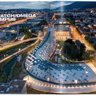 "SWATCH/OMEGA CAMPUS, Design 12.2011–09.2013, Construction 10.2013–09.2019." Beleuchteter, kurviger Gebäudekomplex in Stadt.