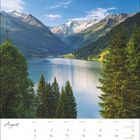 Kalenderblatt für August, umgeben von Bergen und einem See. Bäume im Vordergrund, klare Himmel im Hintergrund.