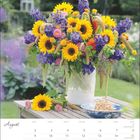 Kalenderseite: August mit einem Bouquet aus Sonnenblumen und violetten Blüten in einer Vase auf einem Gartentisch.
