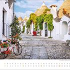 Text "august". Kalender mit rustikalen weißen Häusern, Ziegelsteinstraße, Fahrrad mit Blumen, grüne Pflanzen an Fassaden.